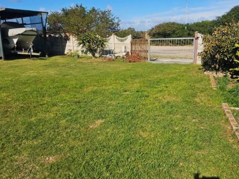 A spacious residential garden featuring a well-maintained lawn, enclosed by a precast concrete boundary wall with both vehicle and pedestrian gate access.
