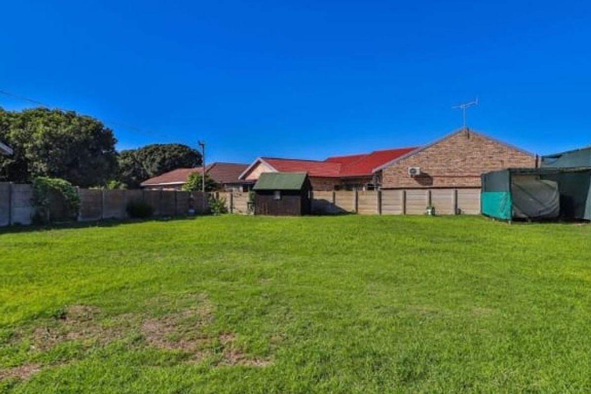 A spacious rear garden featuring a well-maintained lawn, enclosed by precast concrete boundary walls, with a small storage shed on the property.