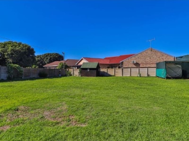 A spacious rear garden featuring a well-maintained lawn, enclosed by precast concrete boundary walls, with a small storage shed on the property.