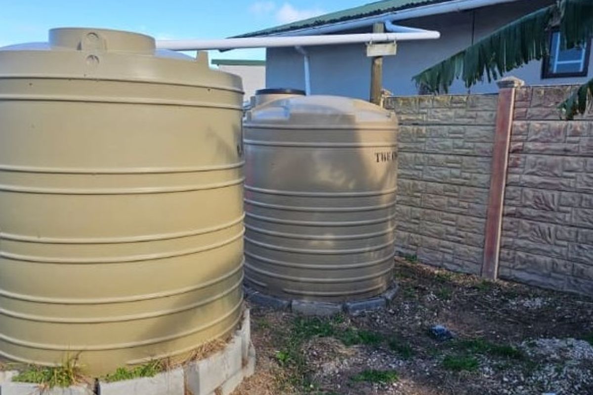 Rear exterior area featuring two large water storage tanks connected to the building's guttering system, set against a precast concrete boundary wall.