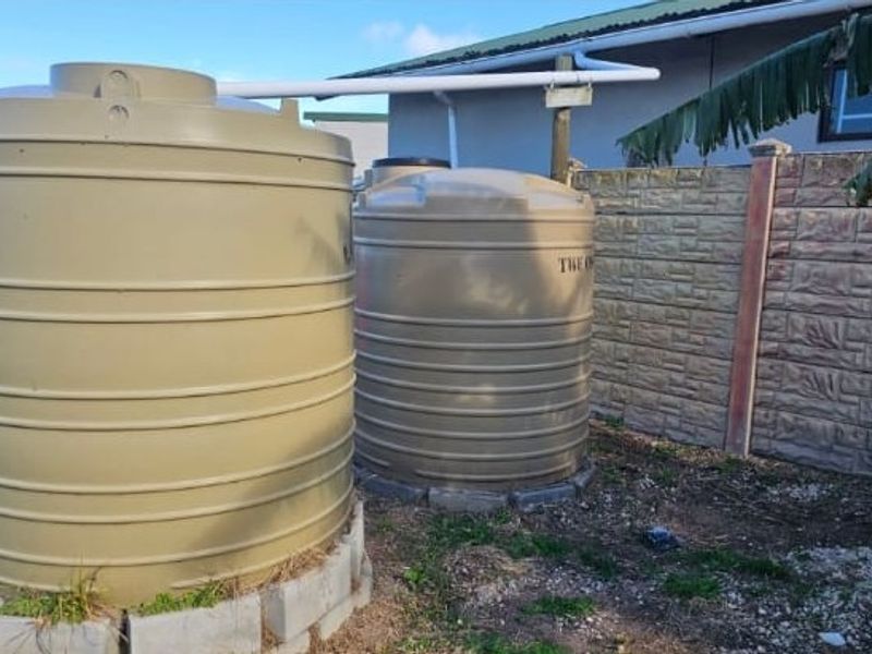 Rear exterior area featuring two large water storage tanks connected to the building's guttering system, set against a precast concrete boundary wall.