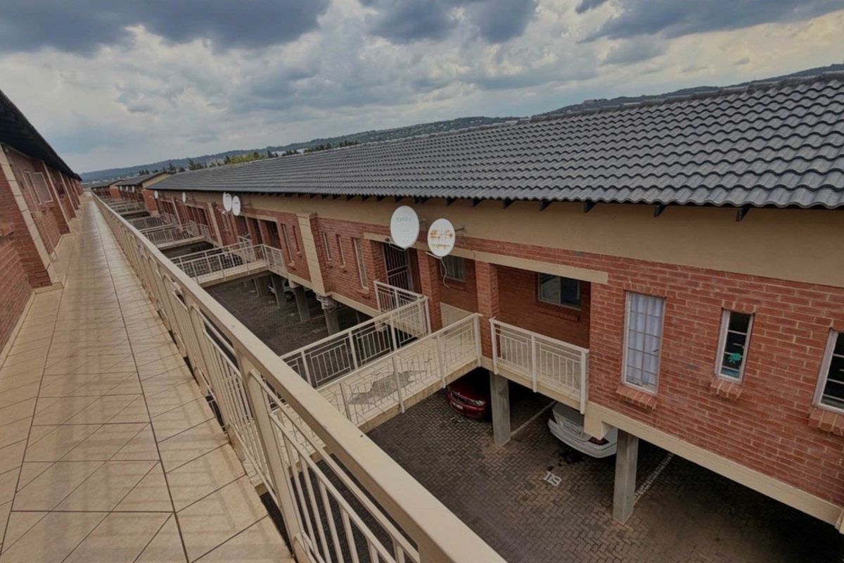 An elevated view of the apartment complex exterior, featuring brick facade construction, tiled roofing, and ground-level paved parking bays.