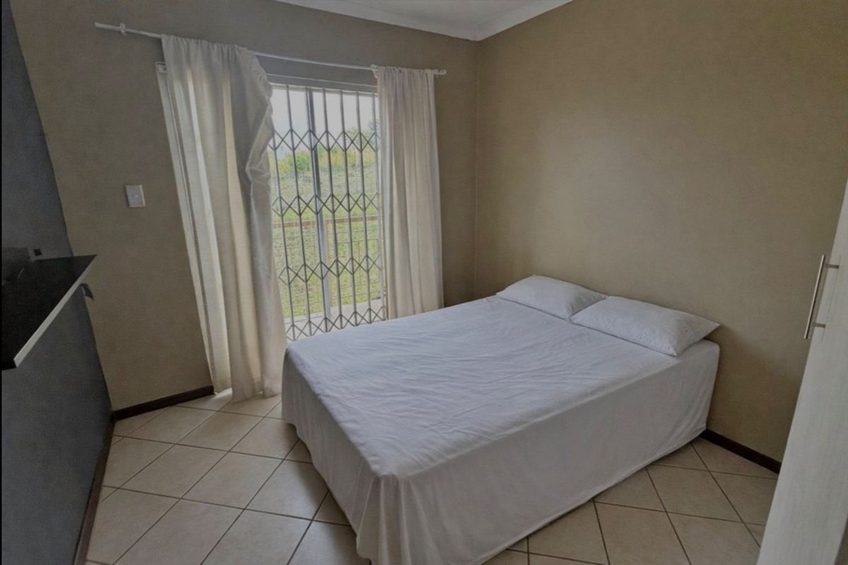 A bedroom featuring tiled flooring, a built-in cupboard, and a sliding glass door with a security gate providing access to the exterior.