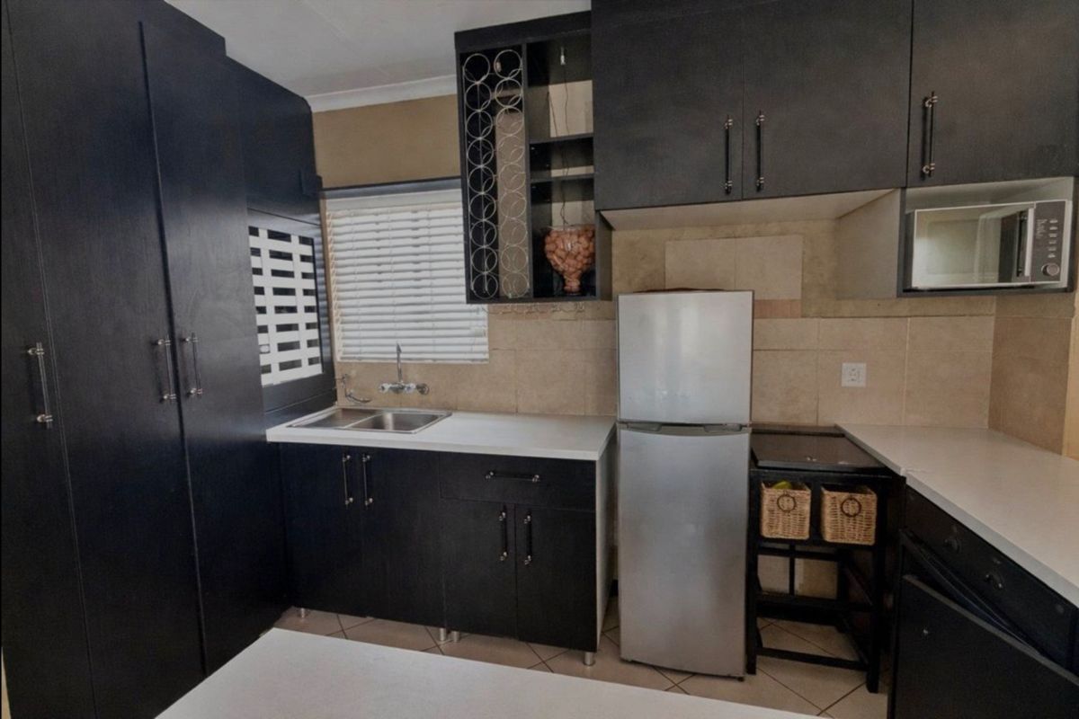 Compact kitchen featuring dark cabinetry, tiled backsplash, double sink, and built-in microwave, offering functional storage and preparation space.