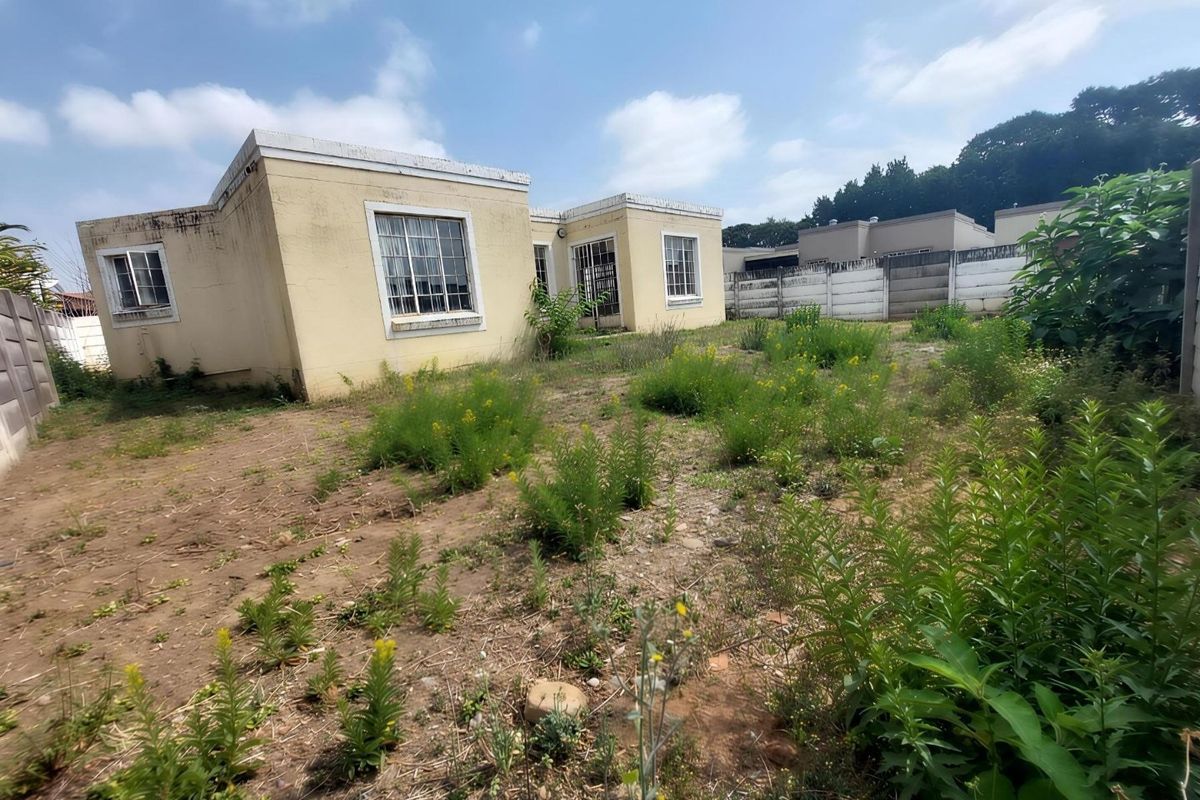 Rear view of the property showing the exterior facade, aluminum windows with security bars, and an unmaintained garden area with boundary walling.