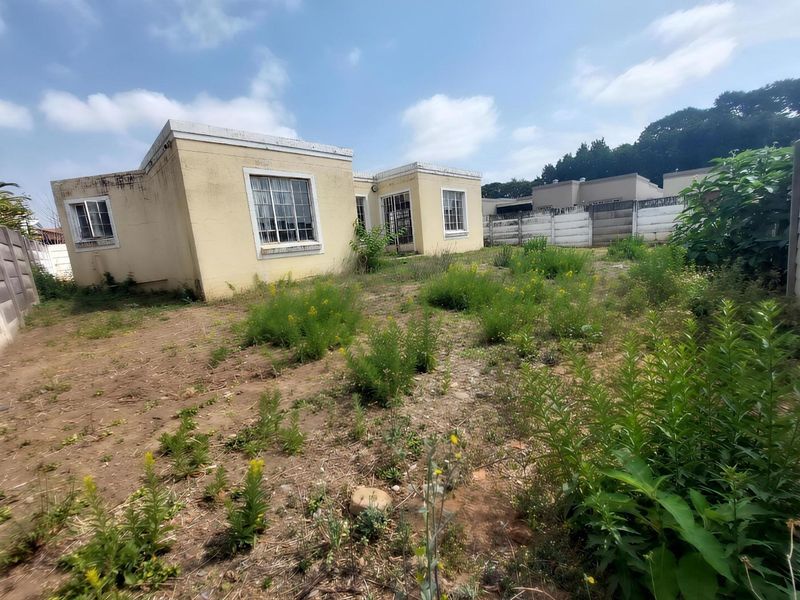Rear view of the property showing the exterior facade, aluminum windows with security bars, and an unmaintained garden area with boundary walling.