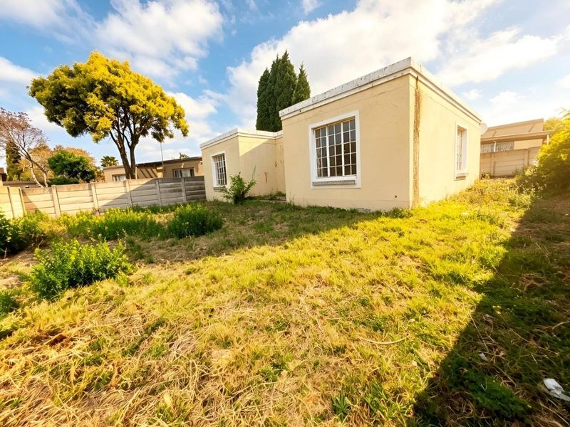 Rear view of the property featuring a large garden area, precast boundary wall, and a structure with grid-pattern windows and a parapet roof.