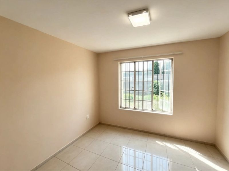 A clean, empty bedroom featuring neutral wall paint, tiled flooring, and a window fitted with security bars.
