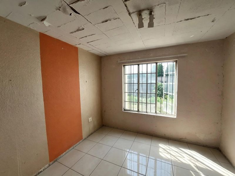 An empty bedroom featuring tiled flooring, security bars on the window, and a ceiling in need of repair and maintenance.