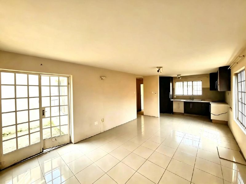 Spacious open-plan living and kitchen area featuring tiled flooring, built-in cabinetry, and direct access to the exterior through french doors.