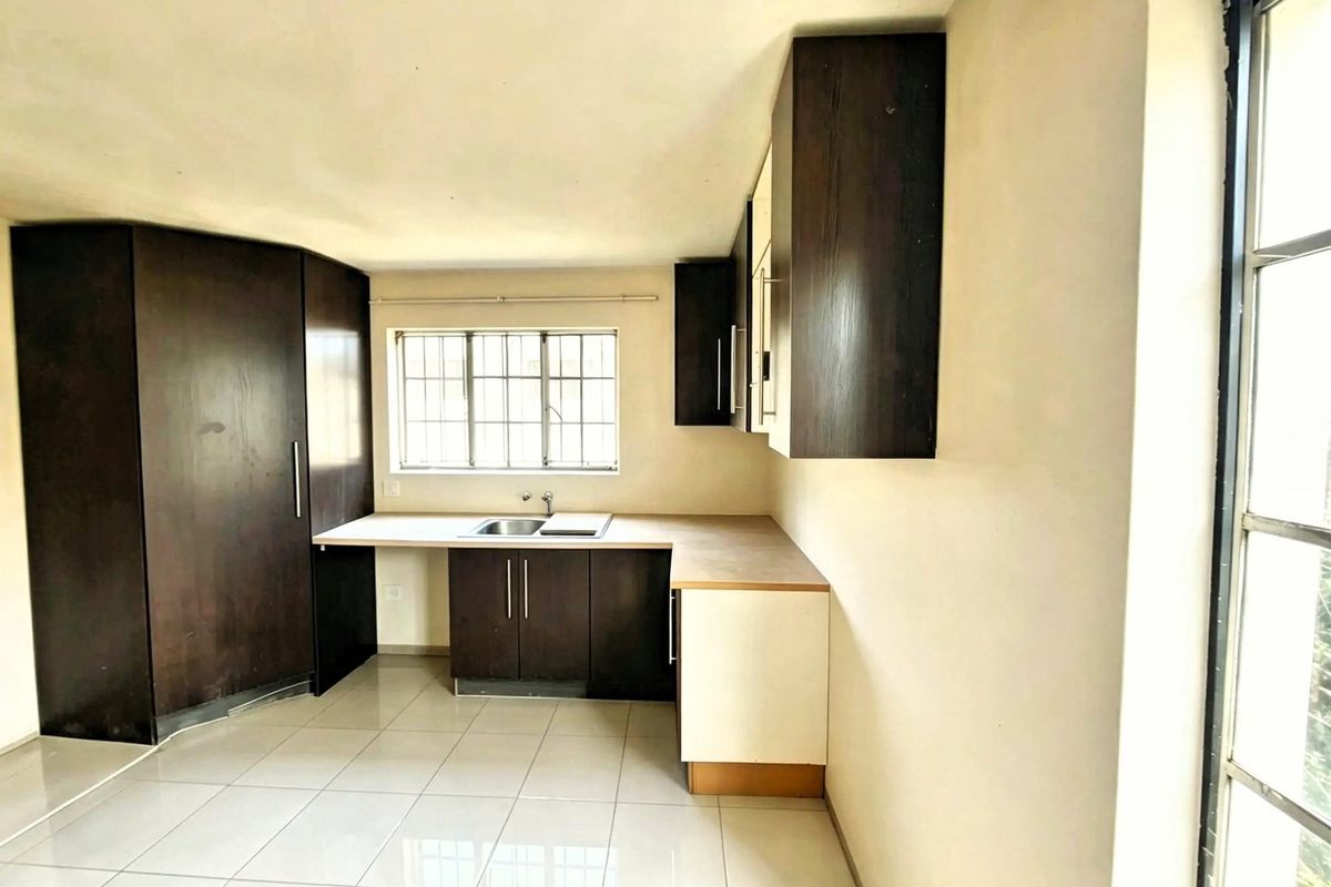 A functional, empty kitchen featuring dark wood-look cabinetry, laminate countertops, a stainless steel sink, and neutral tiled flooring with natural light.