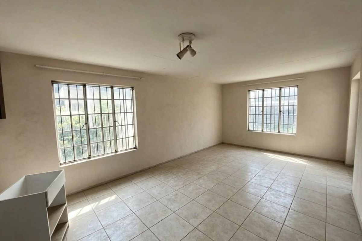 An empty, neutrally painted living area featuring tiled flooring, security bars on the windows, and a ceiling-mounted spotlight fixture.