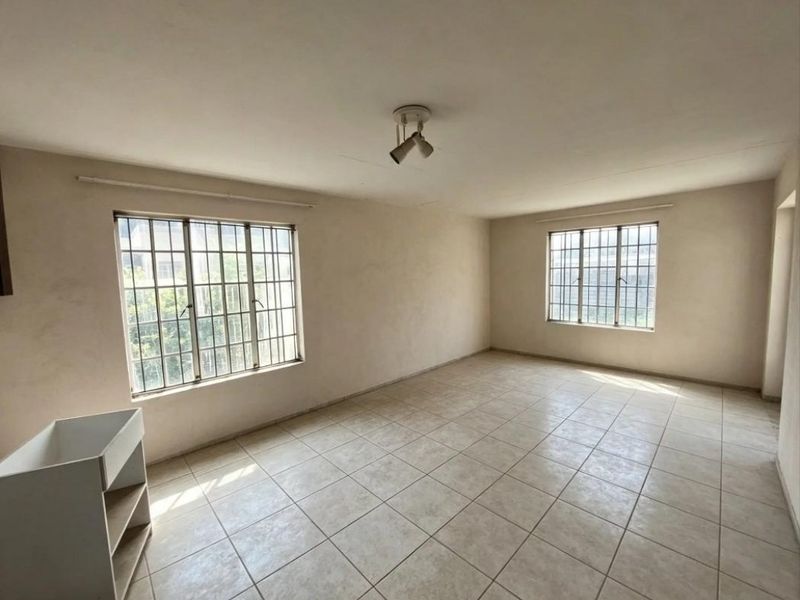 An empty, neutrally painted living area featuring tiled flooring, security bars on the windows, and a ceiling-mounted spotlight fixture.