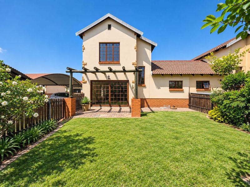 A well-maintained rear exterior view of the townhouse featuring a private garden, brick-paved patio area with a pergola, and secure timber fencing.