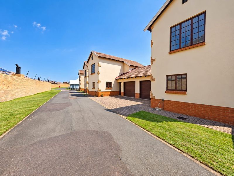 Exterior view of a townhouse complex featuring a paved driveway, double garage, and well-maintained brick and plaster facade.