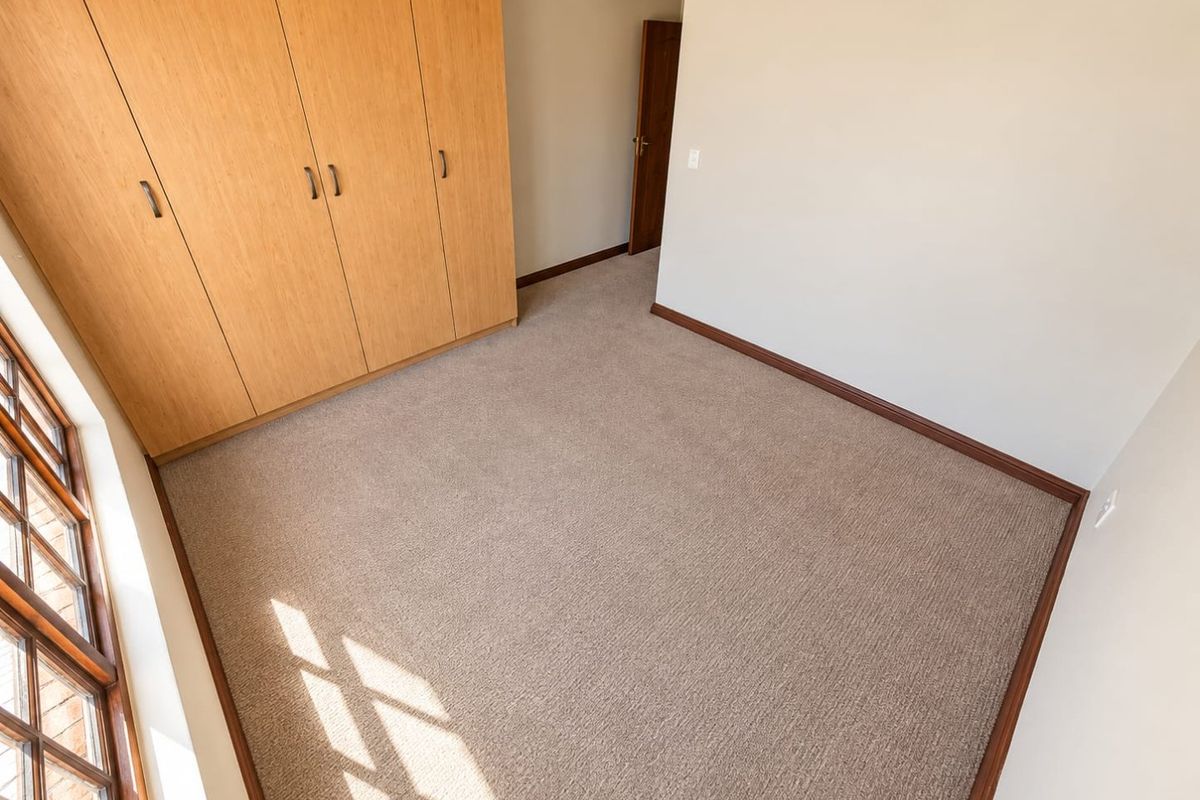 A bright, empty bedroom featuring neutral carpeting, built-in wooden cupboards, and timber-framed windows, offering a clean and versatile space.