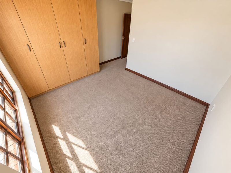A bright, empty bedroom featuring neutral carpeting, built-in wooden cupboards, and timber-framed windows, offering a clean and versatile space.