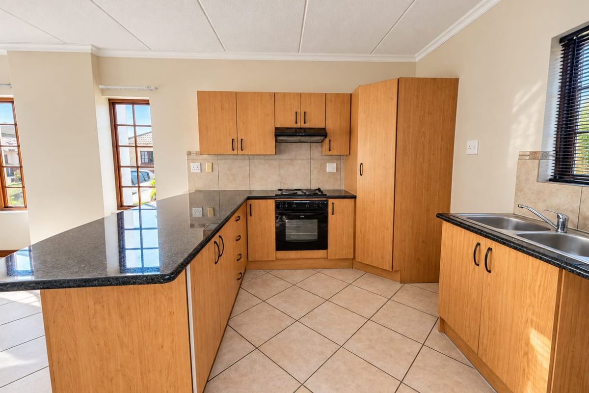 A clean, functional kitchen featuring light wood cabinetry, dark granite countertops, built-in oven, gas hob, and tiled flooring with ample natural light.