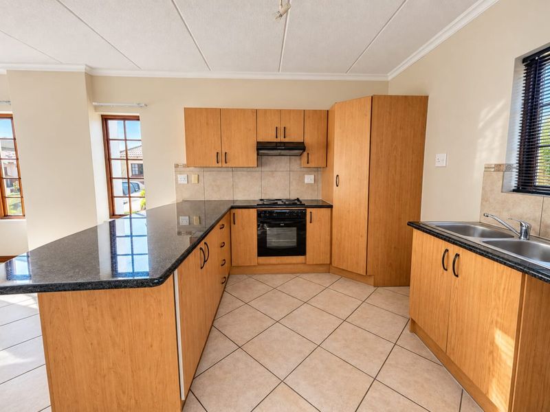 A clean, functional kitchen featuring light wood cabinetry, dark granite countertops, built-in oven, gas hob, and tiled flooring with ample natural light.