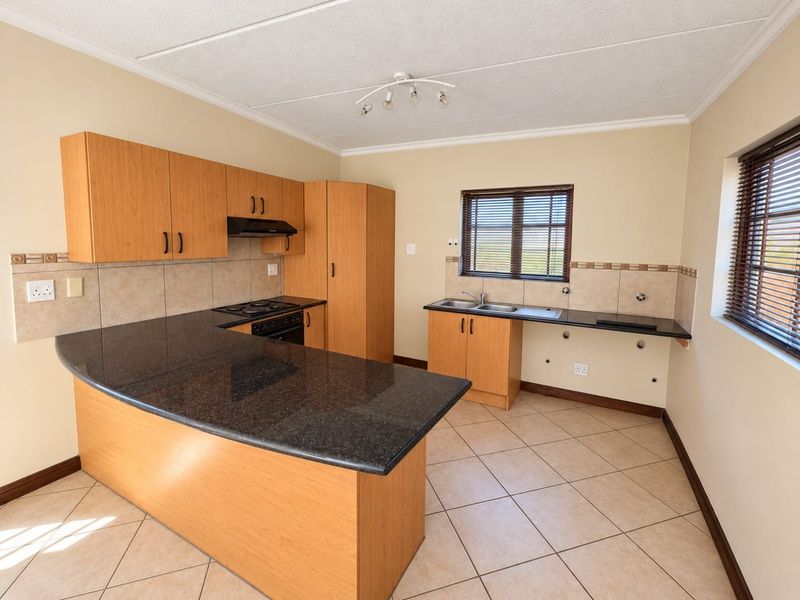 A functional kitchen featuring granite countertops, built-in cabinetry, an electric hob with extractor, and tiled flooring. The space is clean and ready for updates.