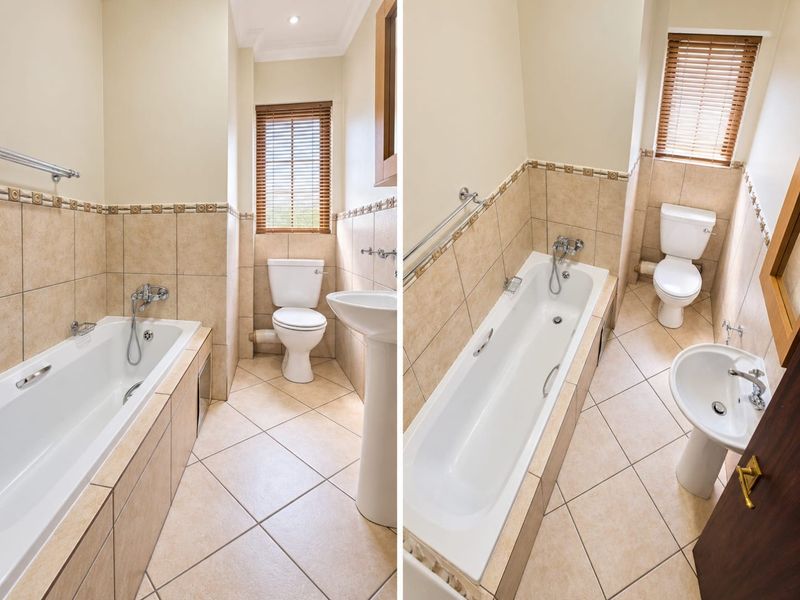 A functional bathroom featuring a pedestal basin, toilet, and bathtub with tiled finishes and natural light from a window with venetian blinds.