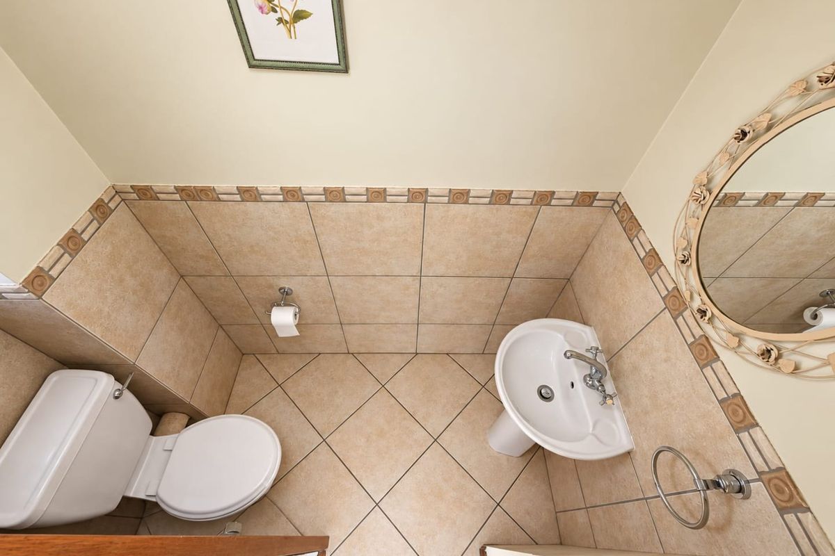 A compact guest bathroom featuring a pedestal basin, toilet, and neutral-toned tiled walls and flooring.