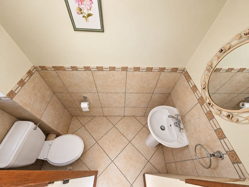 A compact guest bathroom featuring a pedestal basin, toilet, and neutral-toned tiled walls and flooring.