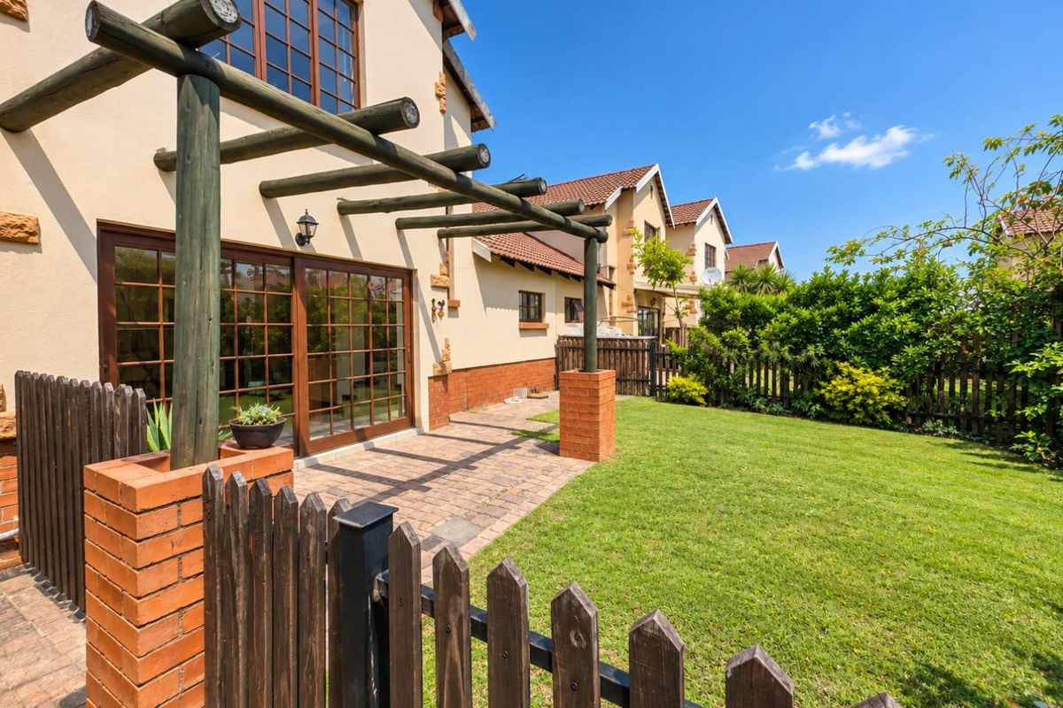 Rear view of the townhouse featuring a private garden, brick-paved patio area with a timber pergola, and wooden fencing.