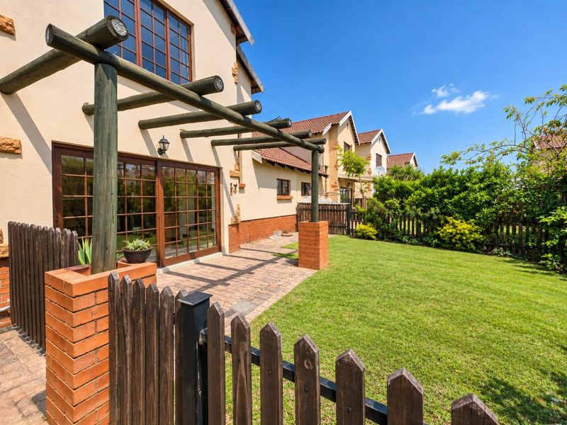 Rear view of the townhouse featuring a private garden, brick-paved patio area with a timber pergola, and wooden fencing.
