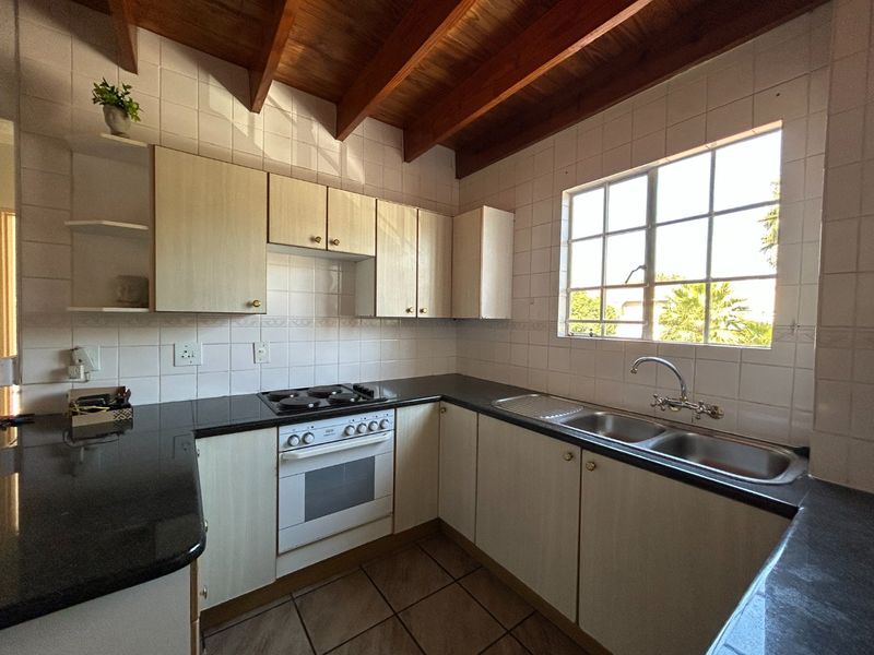 A functional kitchen featuring built-in cabinetry, dark countertops, a built-in oven and hob, double sink, and distinctive exposed timber ceiling beams.