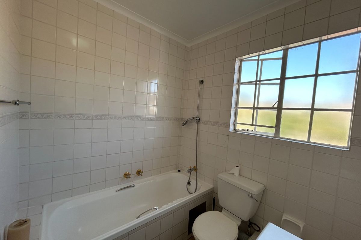 A functional bathroom featuring a built-in bathtub, shower mixer, and toilet, finished with classic white wall tiles and a window for natural light.