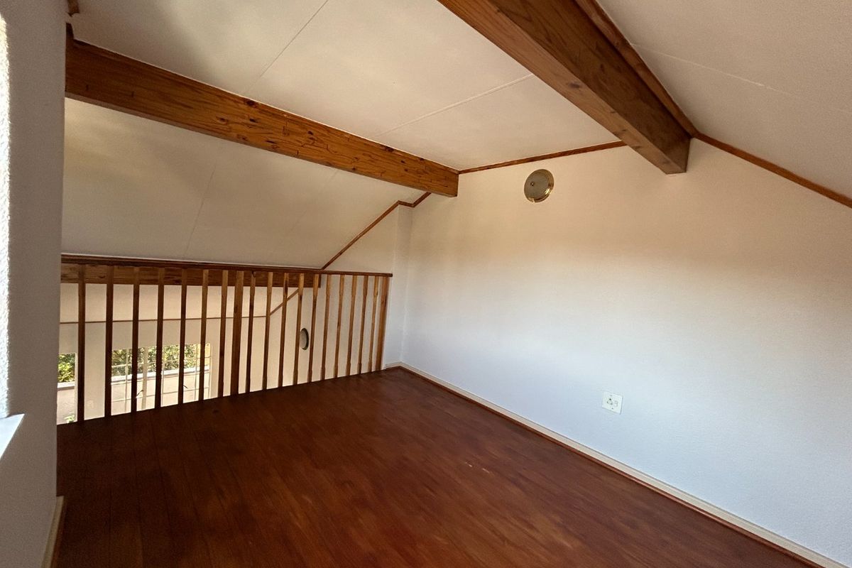 An open-plan loft area featuring exposed timber beams, wooden flooring, and a timber balustrade overlooking the lower level.