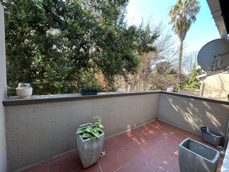 A private balcony featuring terracotta tiled flooring and a solid parapet wall, offering an open outdoor space with surrounding tree views.