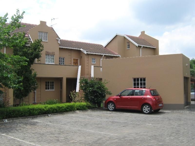 Front elevation of a multi-story apartment complex featuring a paved parking area, stucco exterior walls, and tiled roofing.