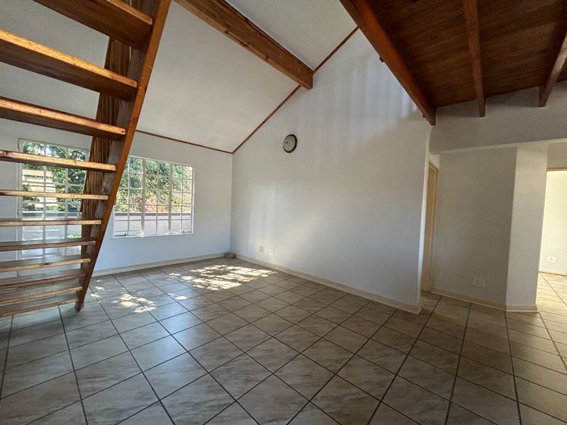 Spacious living area featuring vaulted ceilings with exposed timber beams, tiled flooring, and a wooden staircase leading to an upper level.