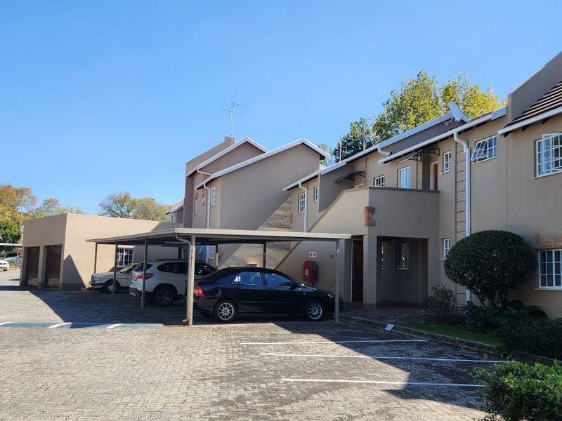 Exterior view of an apartment complex featuring covered parking bays, paved driveway, and multi-story residential units with tiled roofing.