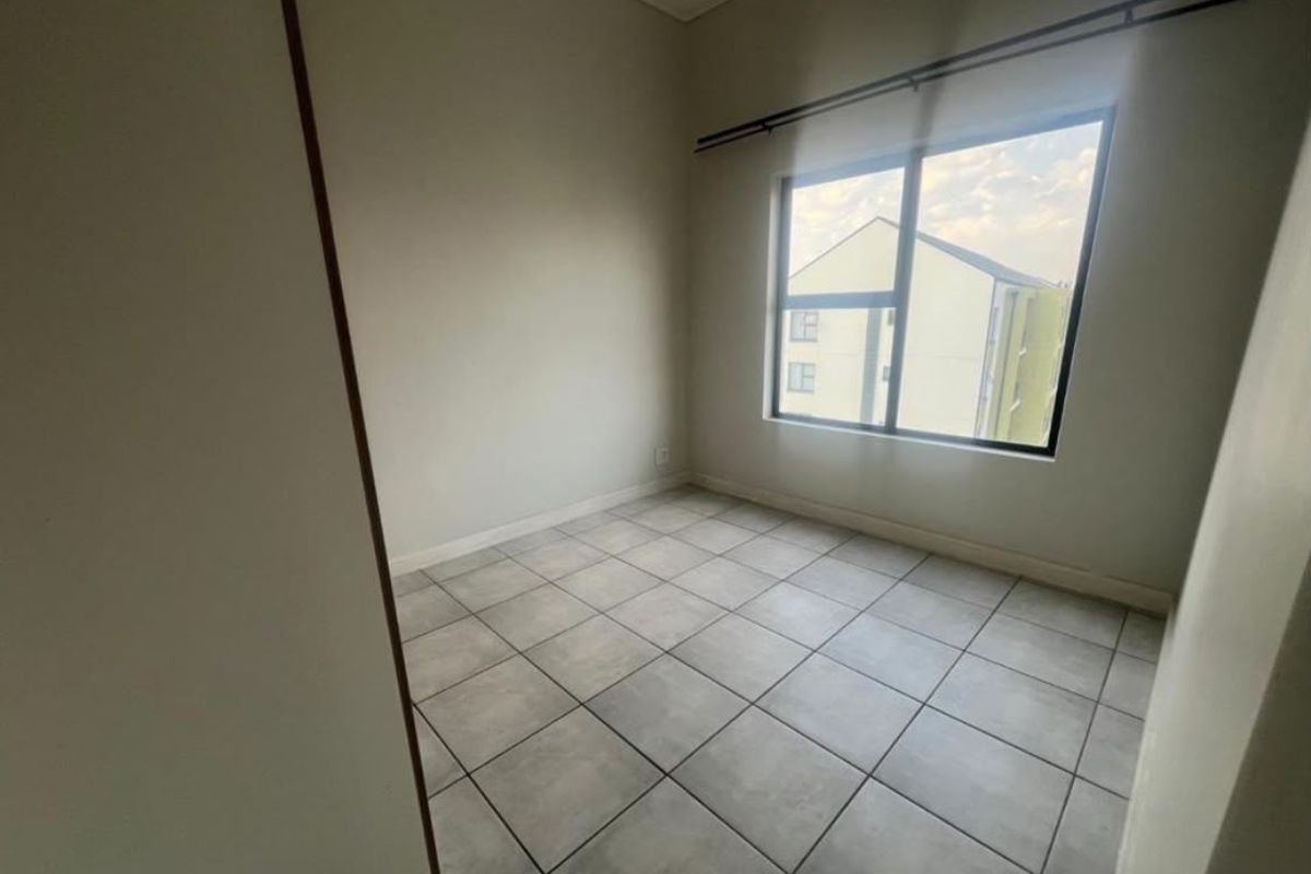 A bright, empty bedroom featuring neutral tiled flooring and a large window with a fitted curtain rod.
