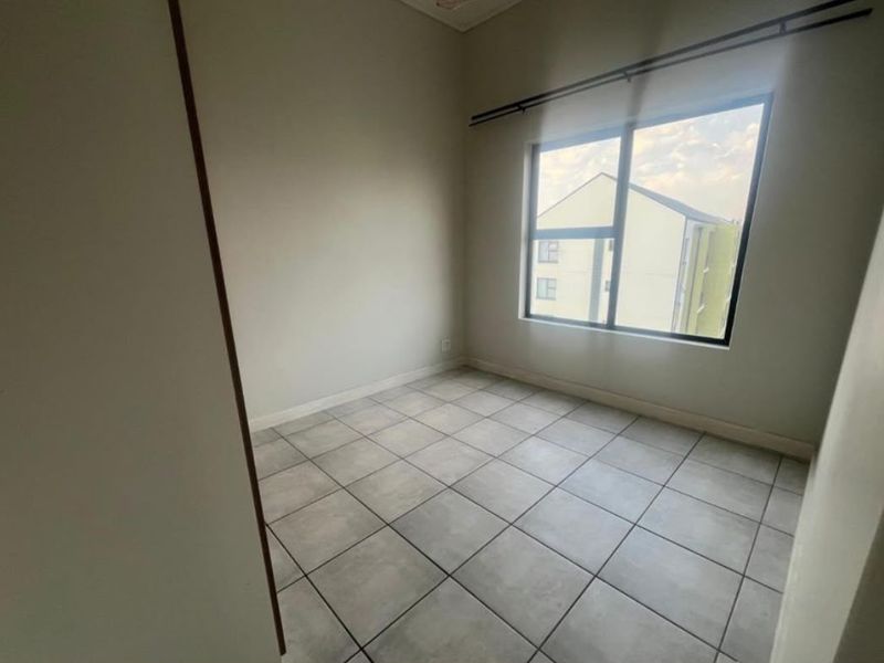 A bright, empty bedroom featuring neutral tiled flooring and a large window with a fitted curtain rod.