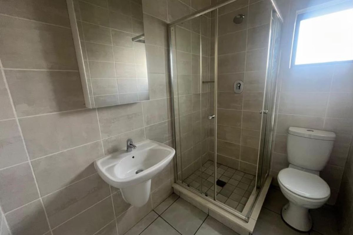 A clean, functional bathroom featuring a wall-mounted basin, a glass-enclosed shower, and a standard toilet with neutral ceramic tiling throughout.