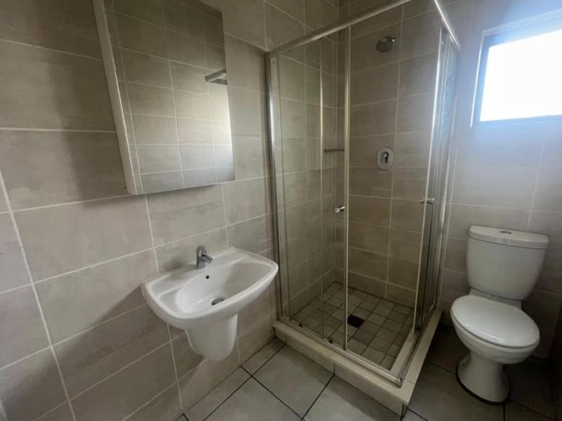 A clean, functional bathroom featuring a wall-mounted basin, a glass-enclosed shower, and a standard toilet with neutral ceramic tiling throughout.