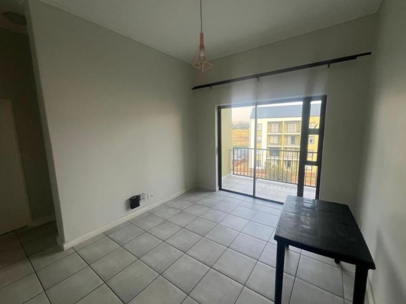 A bright, empty living area featuring neutral tiled flooring, a modern pendant light, and a sliding glass door leading to a private balcony.