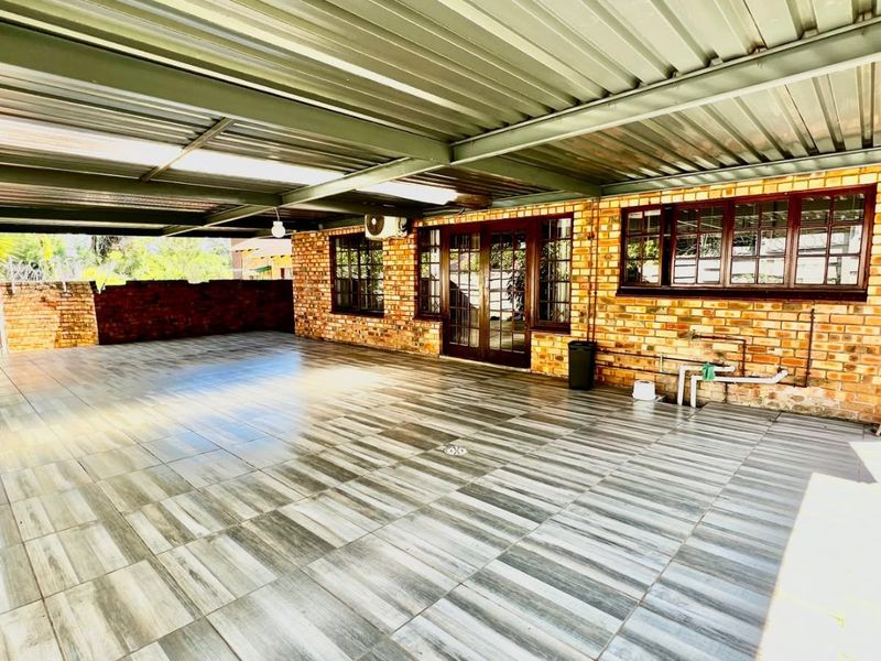 A spacious covered patio featuring modern wood-look tiled flooring, exposed brick walls, and a durable corrugated metal roof, providing a versatile outdoor entertainment area.