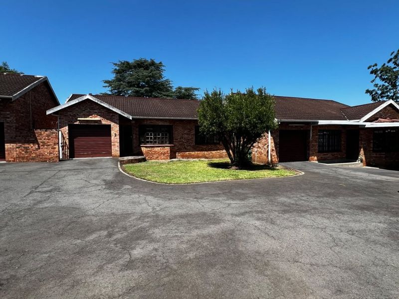 Front exterior view of a brick apartment complex featuring a shared asphalt driveway, tiled roofing, and integrated garage access.