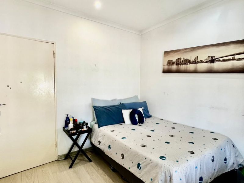 A functional bedroom featuring light-toned laminate flooring, recessed downlighting, and neutral wall finishes, providing a clean and simple living space.