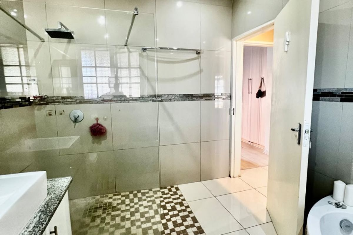 Modern bathroom featuring a glass-enclosed rain shower, granite-topped vanity, and a built-in bathtub with neutral wall and floor tiling.
