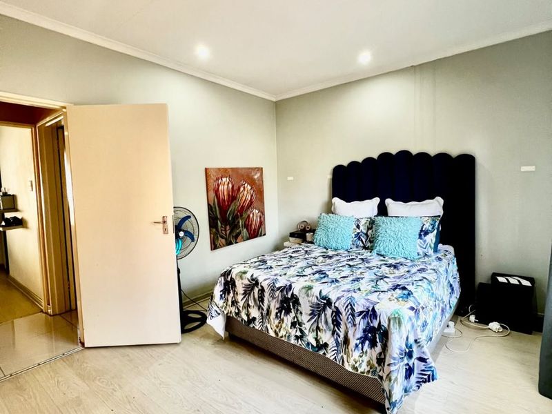 A well-lit bedroom featuring light-toned laminate flooring, recessed downlighting, and a coved ceiling, providing a clean and neutral foundation.