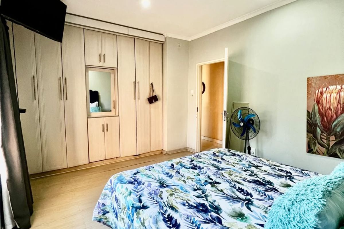 A well-maintained bedroom featuring light-toned laminate flooring, recessed ceiling lights, and extensive built-in cabinetry with a central mirror.