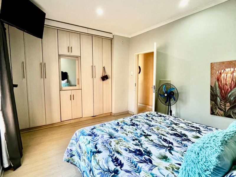 A well-maintained bedroom featuring light-toned laminate flooring, recessed ceiling lights, and extensive built-in cabinetry with a central mirror.