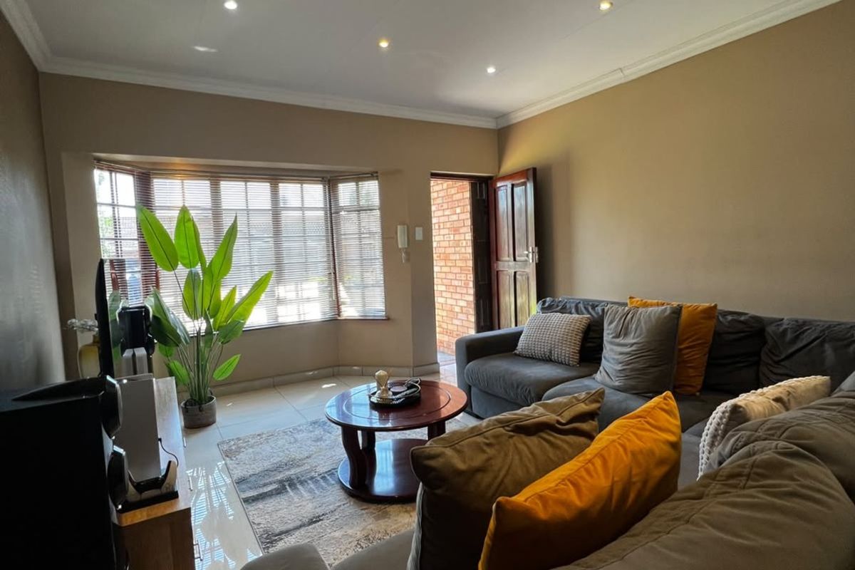 A comfortable living room featuring tiled flooring, recessed downlighting, and a bay window with venetian blinds, providing a bright and functional space.