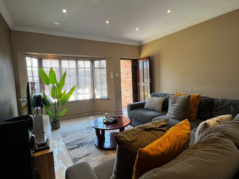 A comfortable living room featuring tiled flooring, recessed downlighting, and a bay window with venetian blinds, providing a bright and functional space.